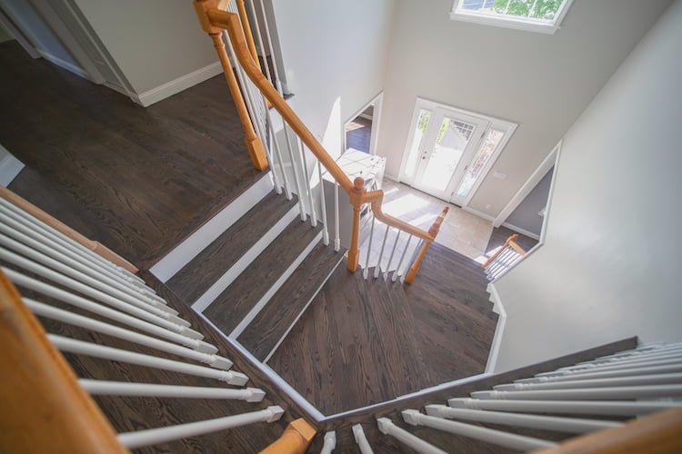 Overhead view of a staircase with dark hardwood floors and a white railing, leading down to an entrance with a door.