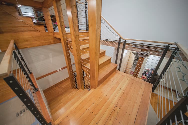 Modern interior staircase with light wood steps and floors, metal railings, and a view into a lower level area, illustrating a contemporary home design.