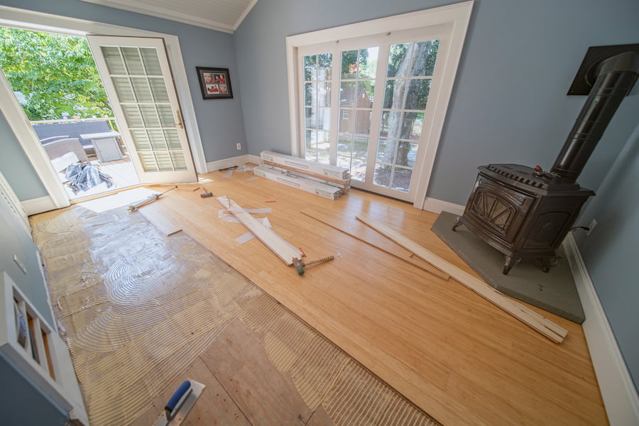 Installation of new hardwood floors in a sunlit room with doors leading to a garden.