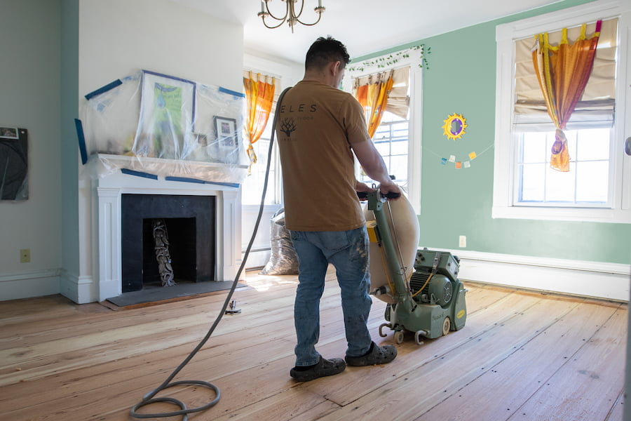 Refinishing of hardwood floors in a spacious attic room with floor sanding equipment present.